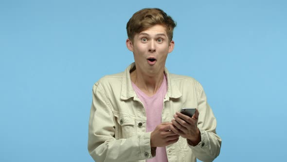 Happy Young Man Looking Surprised at Smartphone Screen Reading Amazing News and Rejoicing Showing