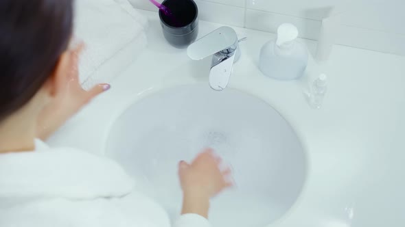 Young Woman in Bathrobe Washing Hands in Deep White Sink