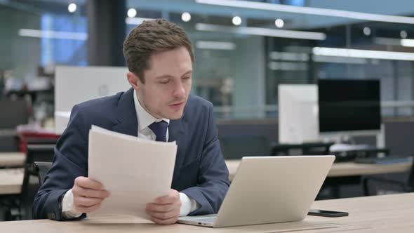 Businessman with Laptop Reading Documents in Office