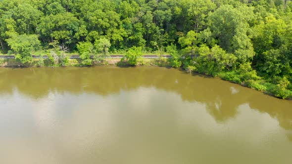 right drone flight over a lake next to a rural country road next to tress in a forest in Illinois 4k