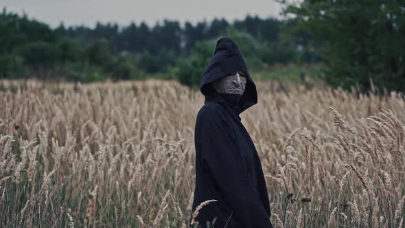 Dark ghost on a wheat field. Back view of a spooky figure in black cloak turning it's scary face