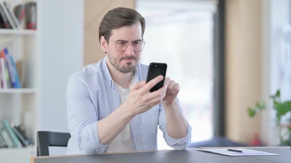 Man in Glasses Reacting to Loss on Smartphone in Office