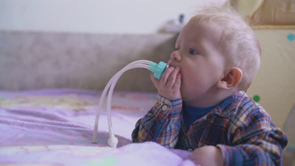 Little Baby in Shirt Nibbles Aspirator at Bed in Room