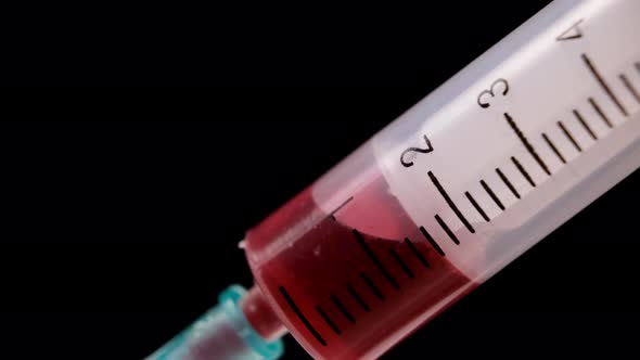 Extreme close-up, drawing blood sample with a medical syringe isolated on black background.