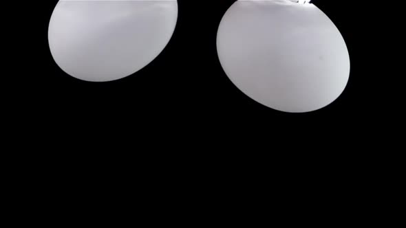Super slow motion fresh white two eggs fall into the water with air bubbles. On a black background.