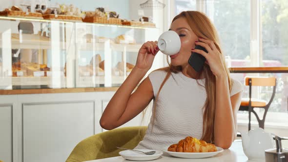 Young Woman Looking Excited, Talking on the Phone While Having Coffee