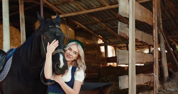 Attractive Girl Caresses the Horse's Black Head and Smiling at a Stable