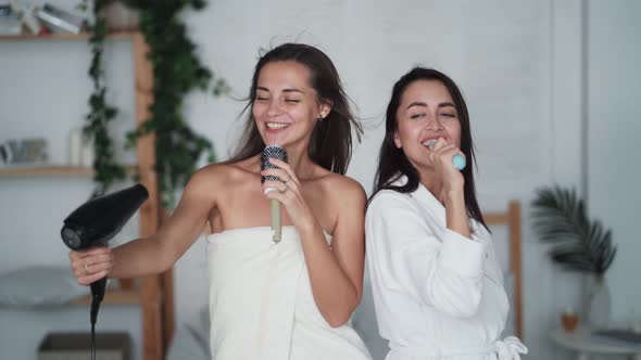 Two Girl Friends in White Bathrobe Dance, Sing and Dry Hair with Hairdryer, Laugh