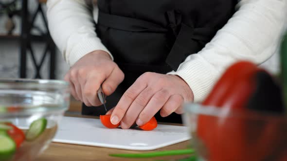 Chef cook man in black apron sliced fresh cherry tomato on board in home kitchen