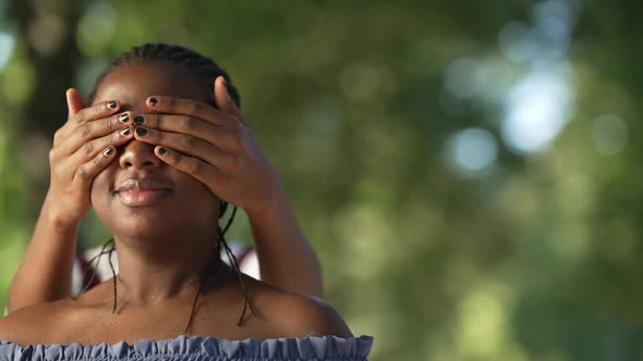 Closeup Young African American Woman Standing in Park As Friend Covering Eyes with Hands