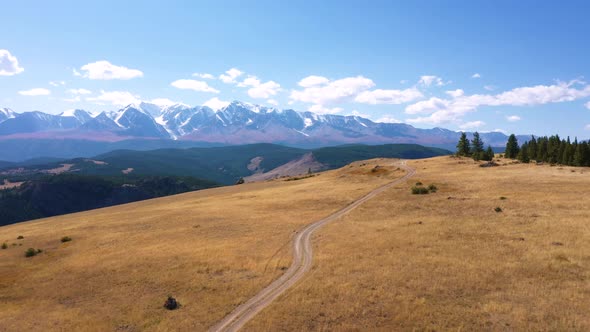 Aerial Flying Over Highway Passing On Hill Against Background Of Snowy Mountains