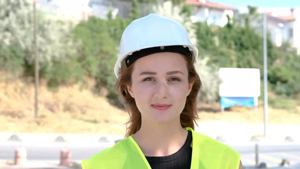 Portrait of an attractive young woman engineer or worker in a uniform and protective white helmet.