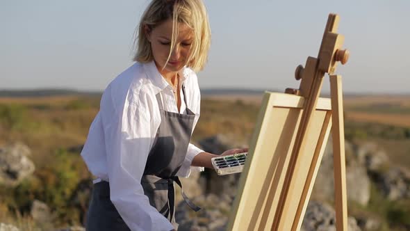 girl artist paints a picture at sunset in the countryside.