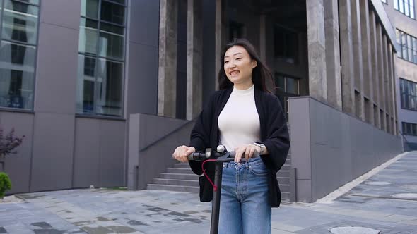 Stylish Young Asian Girl which Riding on Own E-Scooter on the Street Near Beautiful Urban Building