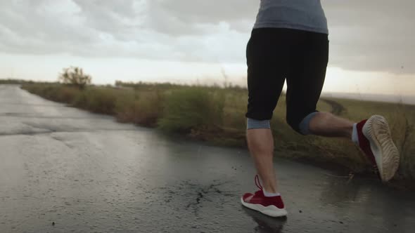 Athlete Runs in Red Sneakers on Asphalt Road in Countryside During Rain Back View