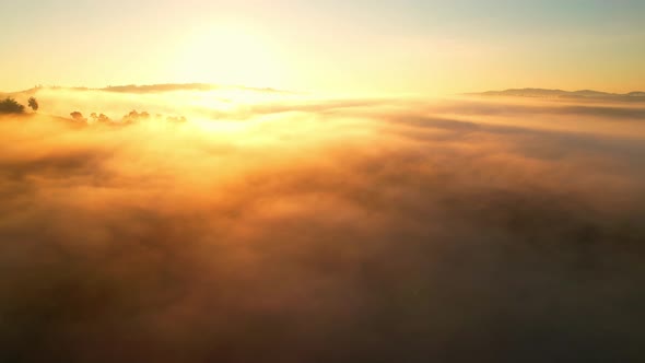 Aerial view of sunrise with fog above mountains. Golden hour and amazing sun rays
