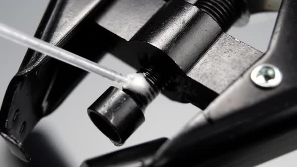 Lubricant spray is sprayed onto a metal mechanical part of black thread press in slow motion. Macro