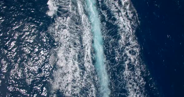 Aerial drone view of man and woman on an inflatable tube towing behind a boat to a tropical island