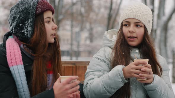 Girls Teenagers Talking Drinking Warm Drinks in a City Park in Snowy Weather