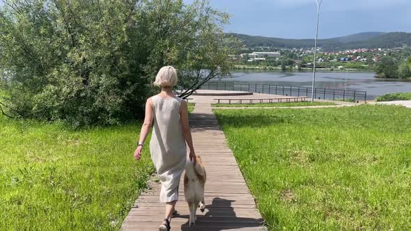 A Girl with an Akita Inu Dog Walks Through the Park to the Lake