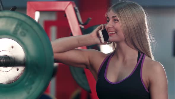 Smiling Fit Woman Talking on the Phone in the Gym Weight Room