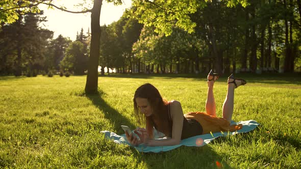 Woman Laying Down Over Green Grass While Typing a Message on Phone