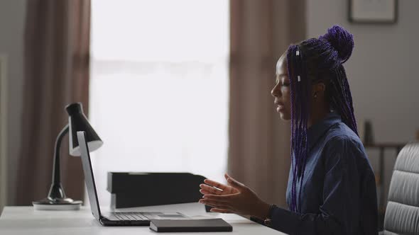 Black Woman is Consulting Online Sitting at Table with Laptop Looking at Web Camera and Answering