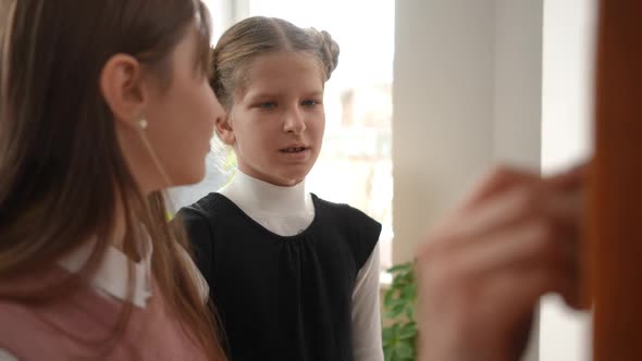 Portrait of Concentrated Schoolgirl Listening to Classmate Explaining Task Standing at Chalkboard