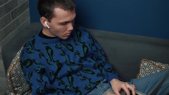 A Focused Young Man Wearing Headphones Working Using His Laptop on Sofa at Home.