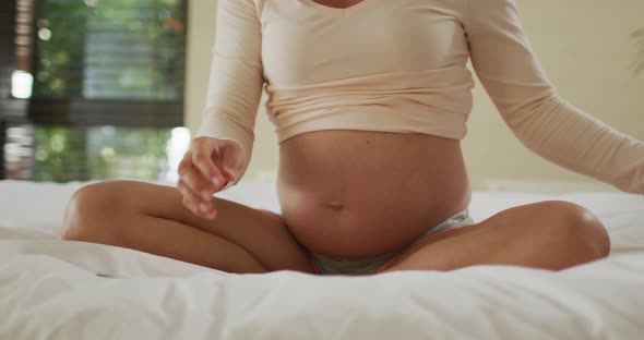 Midsection of caucasian pregnant woman sitting on bed and putting headphones on belly
