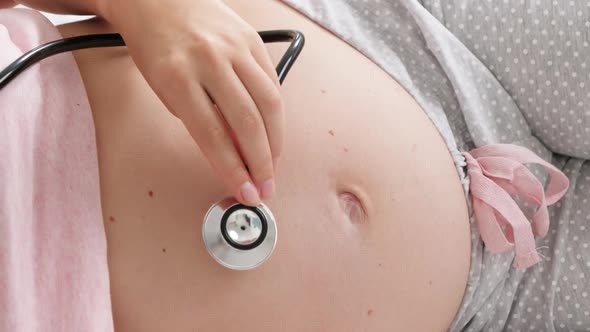 Closeup of Doctor Listening To Baby Heartbeat with Stetschope in Big Belly of Pregnant Woman