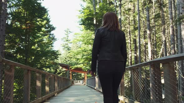 Brunette Woman Strolls on Wooden Road Footbridge in Forest