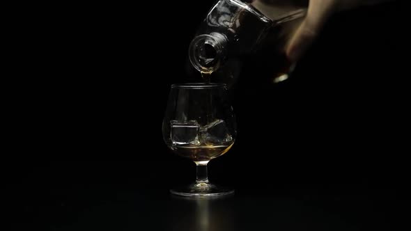 Pouring Alcohol Drink Whiskey, Cognac Into Glass. Black Background. Slow Motion