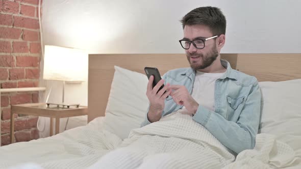 Attractive Young Male Designer Using Smartphone in Bed