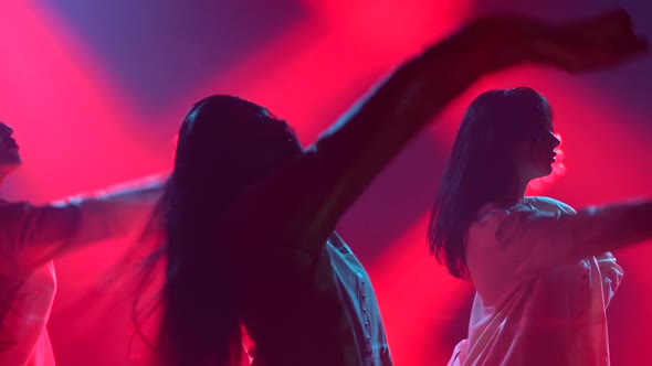 Silhouettes of a Three Charming Womans in White Shirt Are Dancing on the Stage. Shot in a Dark