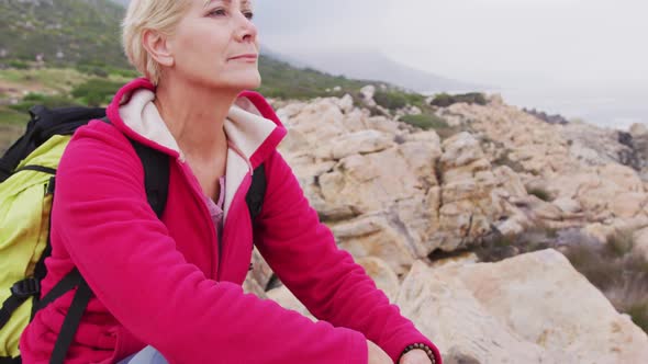 Senior hiker woman with backpack with hand on her chin sitting on the rocks