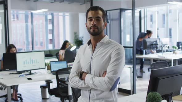 Portrait of mixed race businessman standing in office smiling, with colleagues working in background