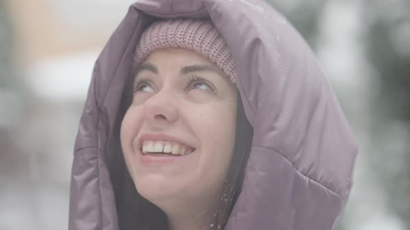 Headshot of Joyful Carefree Beautiful Young Woman with Tongue Out Catching Snowflakes Outdoors