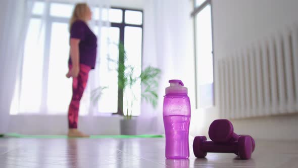 Fitness Training Overweight Woman Squatting on the Yoga Mat Then Walks to a Bottle of Water and Pick