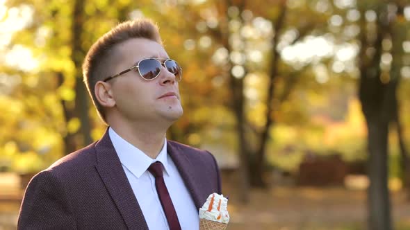 Successful Young Businessman Walks in the Autumn Park and Eats Ice Cream.