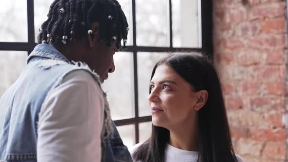 Happy Multiracial Spouses Standing Next to the Window Looking at Each Other and Then Gazing Out of