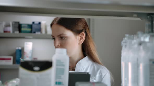 Female Pharmacist Checks Medical Products with a List on a Digital Pad