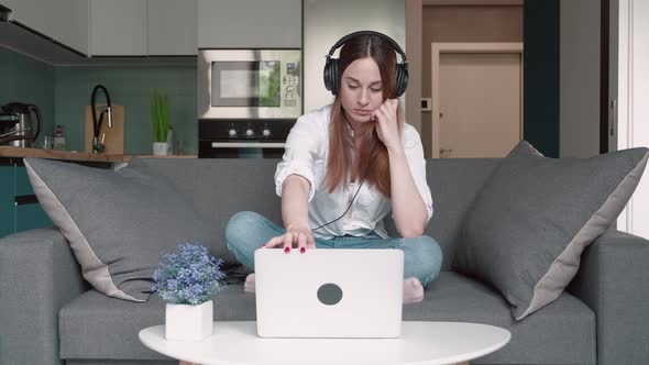 Young Woman Sitting on Couch Using Laptop and Concentrates on Work