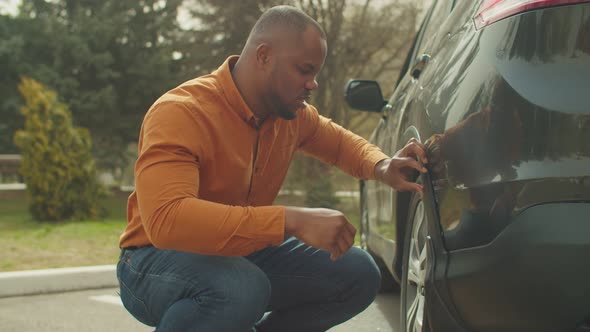 Frustrated African Man Looking at Damaged Scratched Car