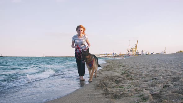 Happy Young Woman Walking with Her German Shepherd Dog Outdoor on the Beach Slow Motion