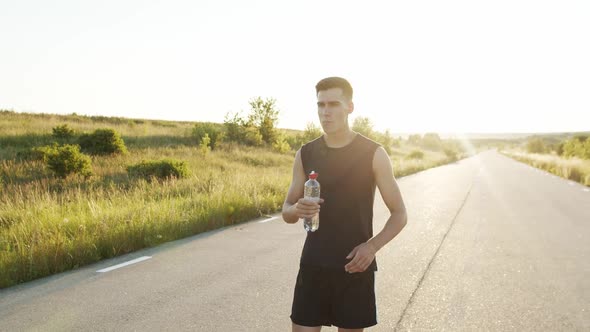 Sportsman Walking on Road at Nature with Sunset and Drinking Water From Bottle