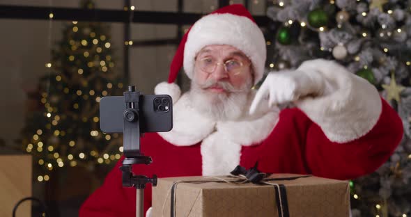 Focus on Smartphone Mounted on Tripod Against the Blurred Background of a Cheerful Santa Claus