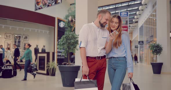 Man and a Woman are Standing in the Mall Looking at the Phone Talking and Laughing