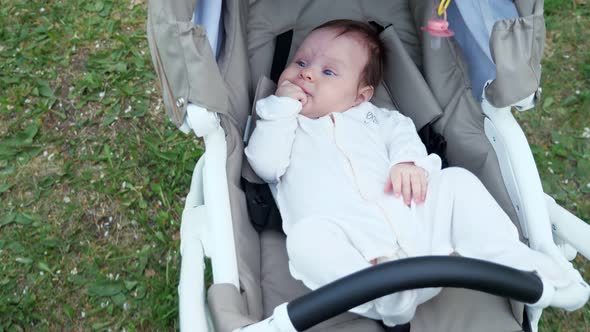 Funny Small Kid in White Overalls Lies in Grey Baby Carriage