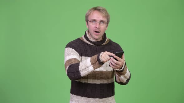 Studio Shot of Blonde Handsome Man Using Phone and Looking Shocked